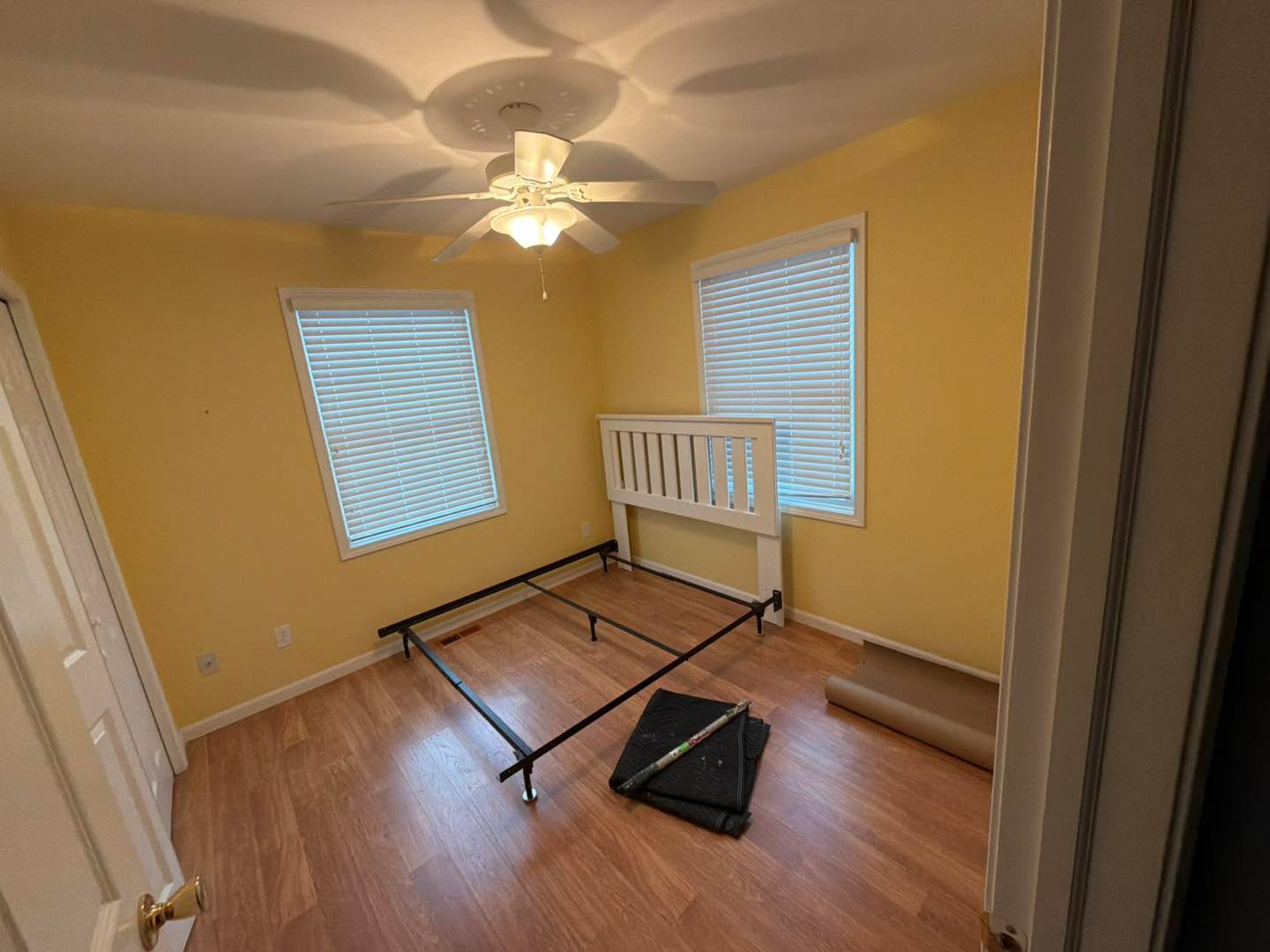 Freshly painted yellow bedroom with white crown molding, ceiling fan, and new flooring — Port Austin residential repaint