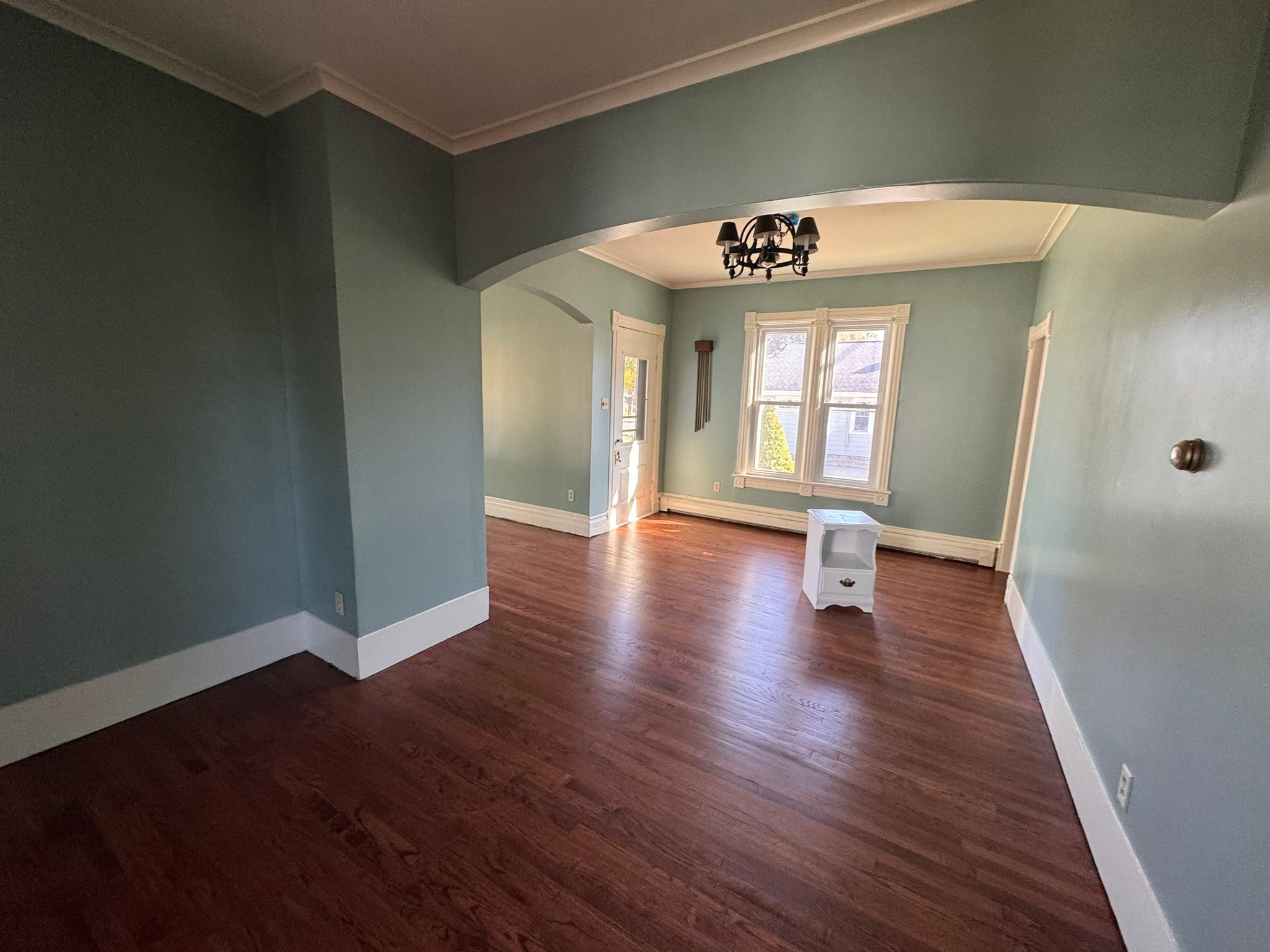 Finished sage green living room with white crown molding, hardwood floors, and chandelier — interior repaint by S&S Home Finishes
