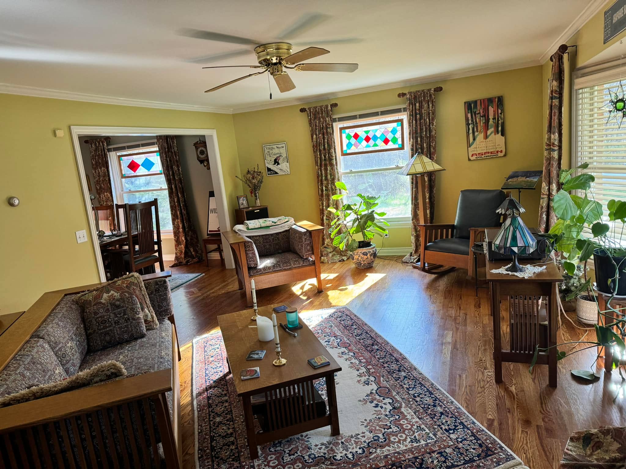 Cozy finished living room with warm yellow walls, stained glass windows, hardwood floors, and Oriental rug — interior repaint